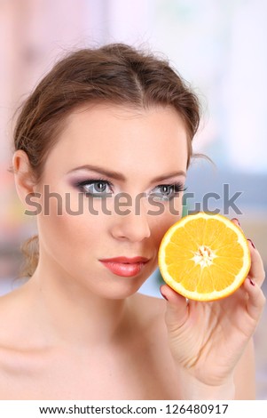 Beautiful young woman with bright make-up, holding orange, on bright background