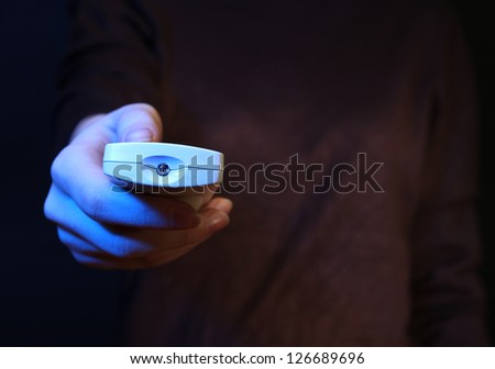 Woman hand holding a TV remote control, on dark background