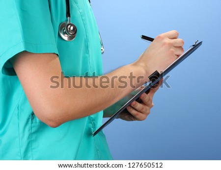 Hand of doctor with pen writing on prescription blank, on blue background