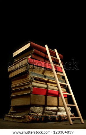 Old books and wooden ladder, on black background