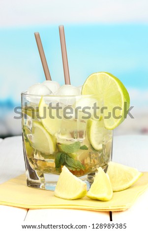 Glass of cocktail with lime and mint on white wooden table on bright background