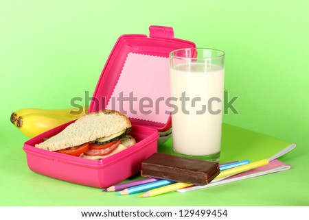 Lunch box with sandwich,bananas,milk and stationery on green background