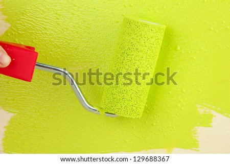Paint roller brush with green paint, on wooden background