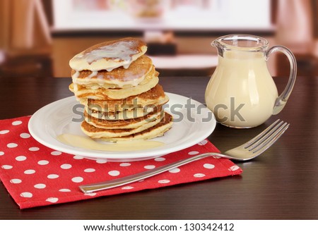 Sweet pancakes on plate with condensed milk on table in room