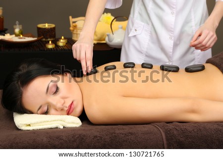 Beautiful young woman in spa salon with spa stones, on dark background