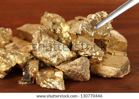 Tweezers holding golden nugget on wooden background
