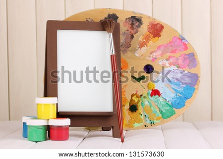 Photo frame as easel with artist\'s tools on wooden background