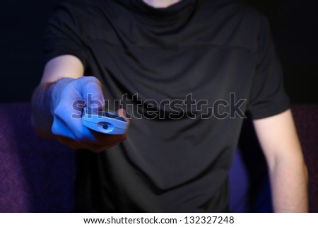 Man hand holding a TV remote control, on dark background