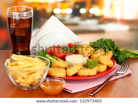 Fried chicken nuggets with vegetables,cola,french fries and sauce on table in cafe