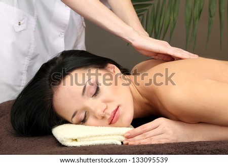 Beautiful young woman in spa salon getting massage, on dark background