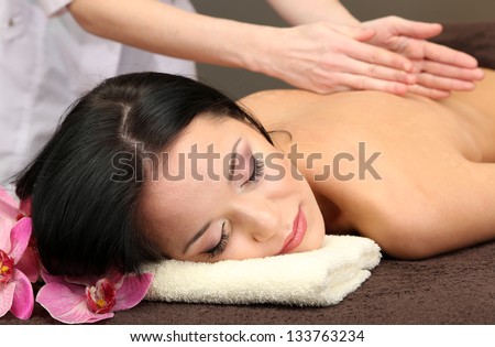Beautiful young woman in spa salon getting massage with spa stones, on dark background