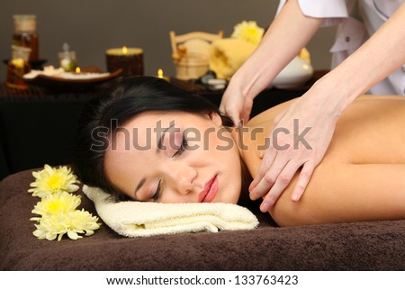 Beautiful young woman in spa salon getting massage, on dark background