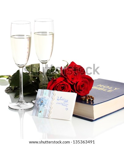 Wedding rings on bible with roses and glasses of champagne isolated on white