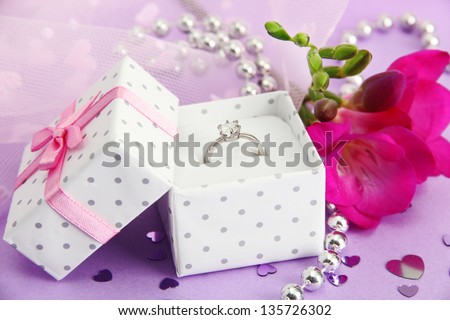 Beautiful box with wedding ring and flower on purple background