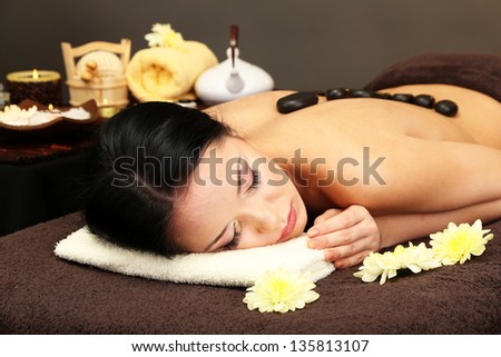 Beautiful young woman in spa salon with spa stones, on dark background