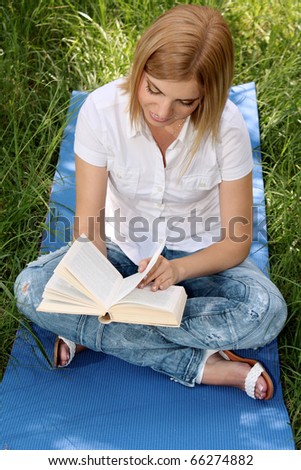 Portrait of young blonde woman reading book in the  park