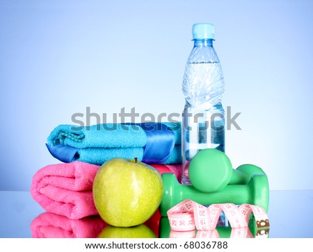 Blue bottle of water, apple, sports towel, measure tape and dumbbells on blue background