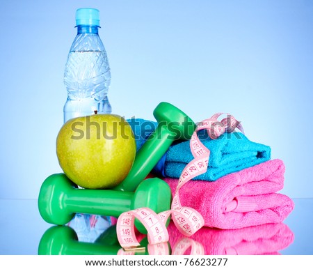 Blue bottle of water, apple, sports towel, measure tape and dumbbells on blue background