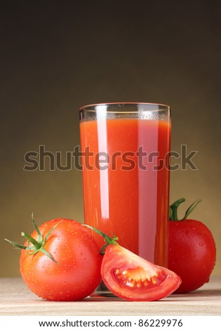 Tomato juice in glass and tomato on wooden table on brown background
