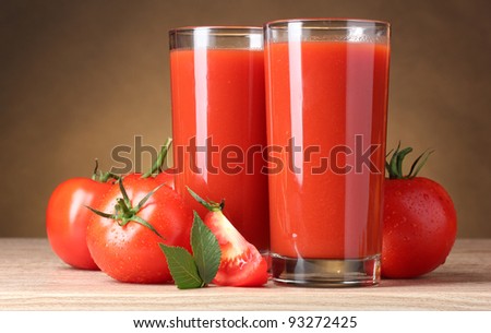 Tomato juice in glasses and tomato on wooden table on brown background
