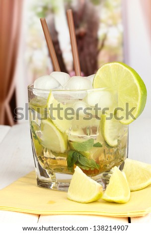 Glass of cocktail with lime and mint on white wooden table on window background