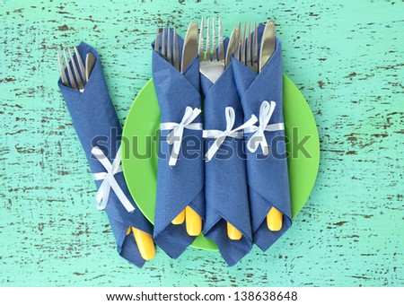 Forks and knives wrapped in blue paper napkins, on color wooden background