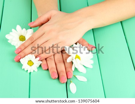 Woman hands with pink manicure and flowers, on color wooden background