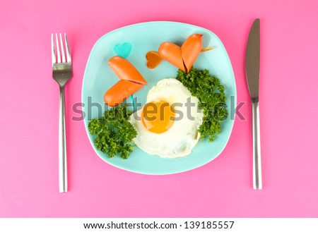 Sausages in form of hearts, scrambled eggs and parsley, on color plate, on color background