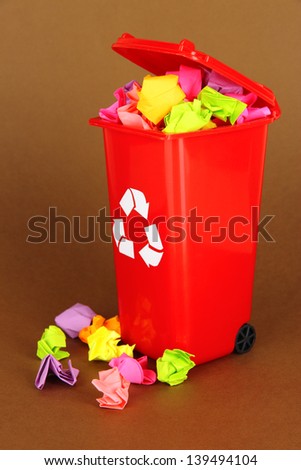 Recycling bin with papers on brown background