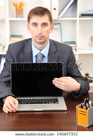 Young businessman with laptop computer facing on his workplace