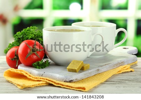 Cups of soup with bouillon cubes on wooden table