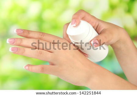 Woman applying cream on hands on bright background