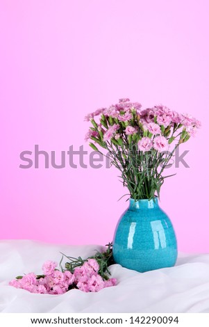Many small pink cloves in vase on white fabric on pink background