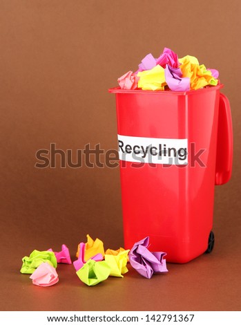 Recycling bin with papers on brown background