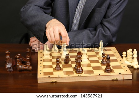 Young business man playing chess on black background