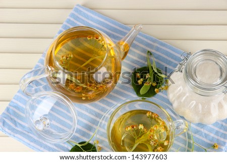 Kettle and cup of tea with linden on napkin on  wooden table