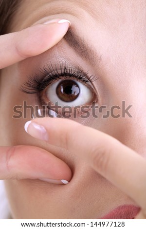 Young woman putting contact lens in her eye close up