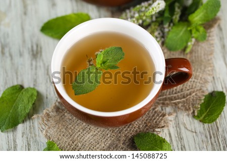 Cup of herbal tea with fresh mint flowers on wooden table