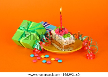 Colorful birthday cake with candle and gifts on orange background