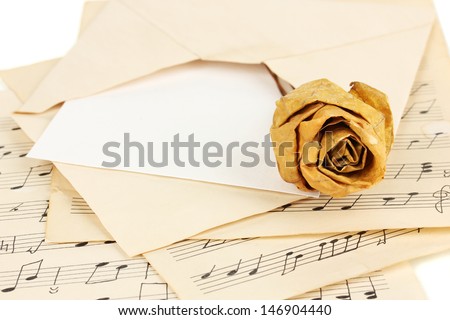 Old envelope with blank paper with dried rose on music sheets close up