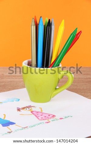 Colorful pencils in cup on table on orange background