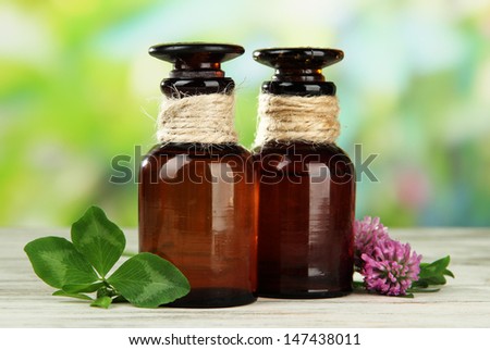 Medicine bottles with clover flowers on wooden table, outdoors