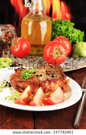 Piece of fried meat on plate on wooden table on fire background