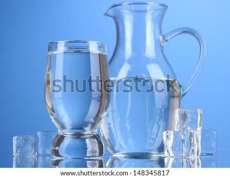 Glass pitcher of water and glass on blue background