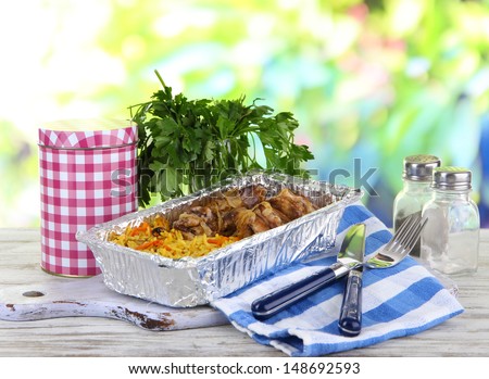 Food in boxes of foil on napkin on wooden board on wooden table on nature background