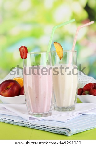 Delicious milk shakes with strawberries and peach on wooden table on natural background