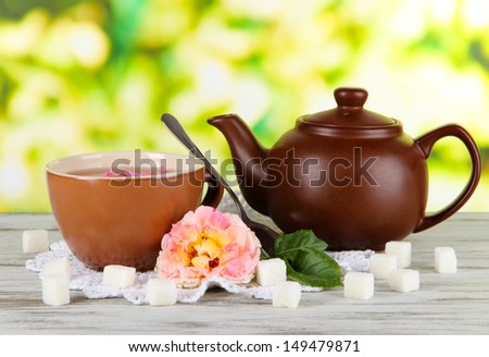 Kettle and cup of tea from tea rose on board on napkin on wooden table on nature background