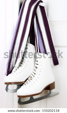 Figure skates hanging on a door knob with scarf
