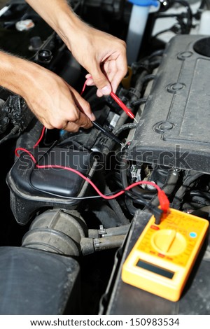 Auto mechanic uses multimeter voltmeter to check voltage level in car battery