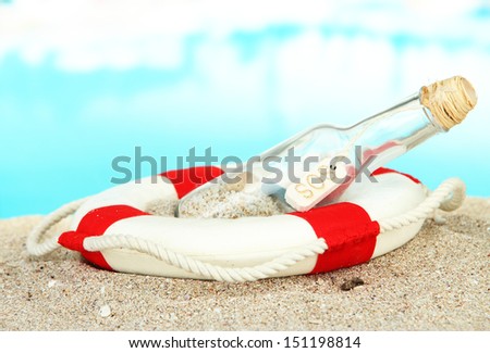 Glass of bottle with note inside on  sand, on bright blue background